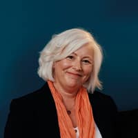 Smiling woman with white hair and orange scarf.