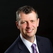 Smiling man in suit with dark background.